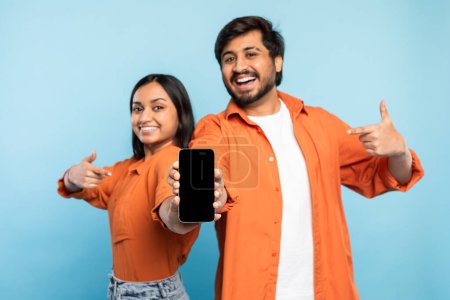 Photo for Playful indian couple points at a smartphone, with individual holding and showcasing the device to the camera - Royalty Free Image