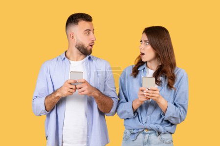 Photo for Both man and woman show shocked expressions as they look at their smartphones, suggesting alarming news or messages - Royalty Free Image