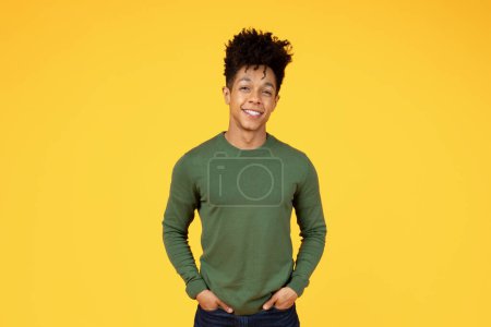 Téléchargez les photos : Un jeune homme noir joyeux portant une chemise verte se tient avec ses mains dans ses poches sur un fond jaune vif - en image libre de droit
