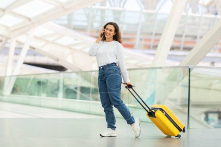 Busy woman traveler with suitcase engaging in a phone conversation while pacing through the airport