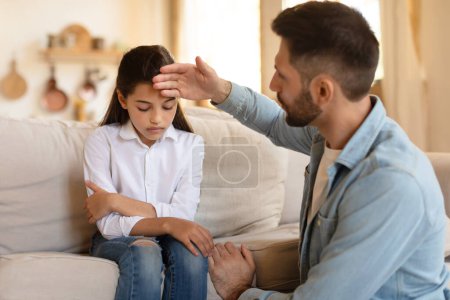 Photo for A caring father touches his daughters forehead, checking for a fever, expressing concern and care - Royalty Free Image
