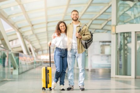 Foto de Sonriente joven pareja caminando de la mano en un corredor del aeropuerto significa la alegría de viajar juntos - Imagen libre de derechos