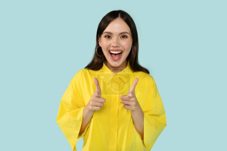 Photo for Hey you. Playful happy beautiful young brunette hispanic woman wearing casual yellow outwear pointing at you and smiling at camera. Cheerful lady flirting on blue studio background - Royalty Free Image