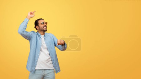 Foto de Un hombre indio alegre con atuendo casual bailando con emoción contra un vibrante telón de fondo amarillo, expresando felicidad y energía - Imagen libre de derechos
