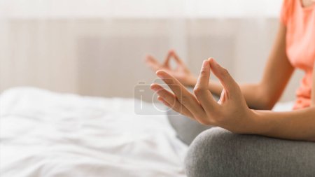 Foto de Mujer haciendo yoga pose de loto en la cama después de despertarse por la mañana, primer plano, espacio de copia - Imagen libre de derechos