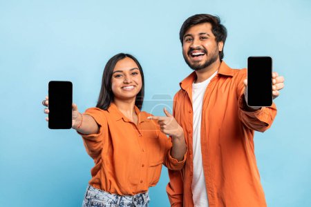 Téléchargez les photos : Couple indien joyeux en orange partageant un moment avec les téléphones mobiles montrant des écrans vides - en image libre de droit