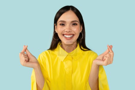 Photo for I Love You. Portrait of beautiful smiling young woman making Asian Korean finger mini heart gesture on blue background. Excited millennial lady showing like sign crossing fingers posing at studio - Royalty Free Image