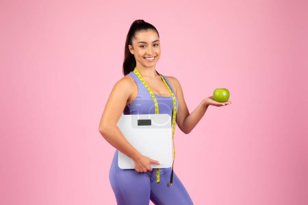 Mujer en forma que sostiene una balanza de pesaje y una manzana verde, lo que significa el control de peso