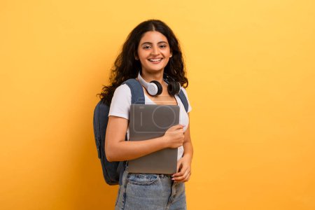 Happy student with headphones around neck holding a laptop, portrays a mix of education and technology