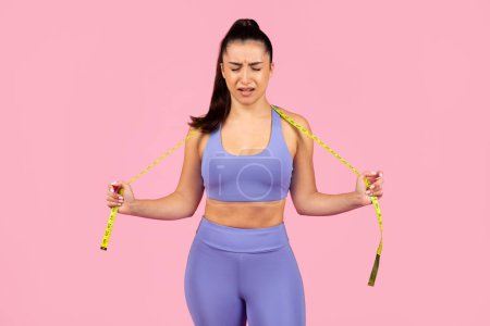 Una joven en ropa deportiva parece angustiada midiendo su cintura con una cinta métrica