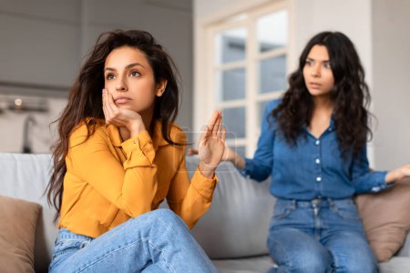 Foto de Mujer joven ofendido en un top amarillo parece molesto mientras conversa con otra amiga en una camisa azul - Imagen libre de derechos