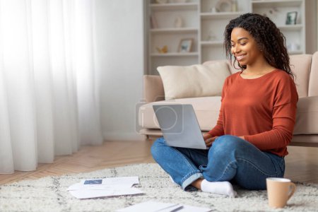 Photo for Black woman sitting on the floor, focusing on a laptop screen. african american female intent on her work or task at hand, working online from home - Royalty Free Image