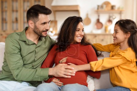 Foto de Una familia alegre con un padre, una madre embarazada y una hija disfrutando de un tiempo de calidad juntos en un ambiente acogedor en el hogar - Imagen libre de derechos