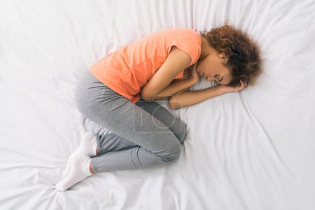 Téléchargez les photos : Femme afro-américaine dormant, se blottissant dans le lit, vue sur le dessus - en image libre de droit