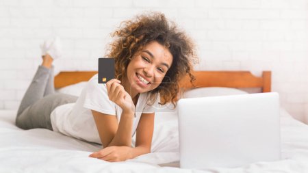 Photo for African-american woman doing online shopping, lying on bed in the bedroom - Royalty Free Image