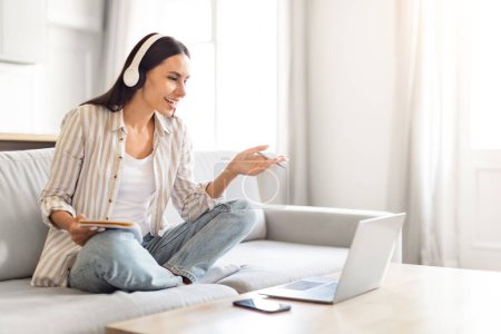 Assise devant son ordinateur portable, une femme gesticule joyeusement lors d'un appel vidéo, exprimant son engagement et son bonheur, copiant l'espace
