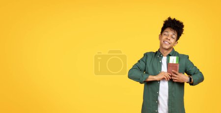 Foto de Un joven afroamericano alegre con el pelo rizado, sosteniendo un pasaporte con una tarjeta de embarque sobre un fondo amarillo - Imagen libre de derechos