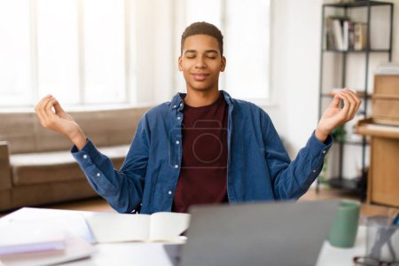 Photo for Calm black teenage student guy practices mindfulness meditation at his study desk with closed eyes, seeking peace amidst busy academic schedule - Royalty Free Image
