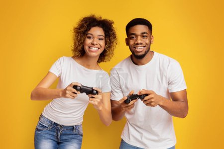 Téléchargez les photos : Jeu couple afro-américain jouant jeu vidéo avec joysticks, fond studio orange - en image libre de droit
