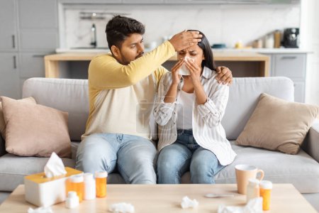 Téléchargez les photos : L'homme indien touche tendrement le front des femmes, vérifiant la fièvre alors qu'elle se mouche, toutes deux entourées de remèdes contre le rhume. - en image libre de droit