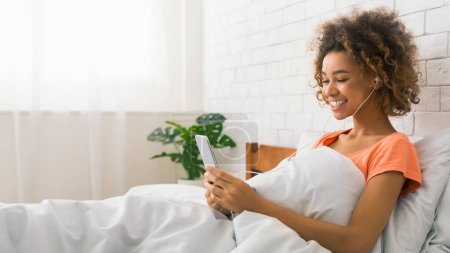 Téléchargez les photos : Happy lady textos sur smartphone, écouter de la musique au lit le matin, espace libre - en image libre de droit