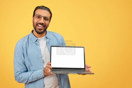 Homme indien tenant un ordinateur portable ouvert avec un écran blanc vierge, parfait pour l'insertion graphique
