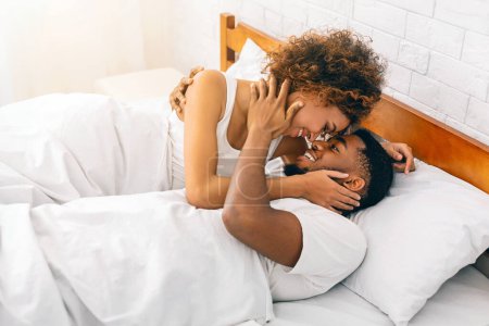 Téléchargez les photos : Dans un cadre confortable de chambre à coucher, un couple afro-américain joyeux bénéficie d'une étreinte aimante, affichant chaleur et confort - en image libre de droit