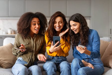 Foto de Mujeres multirraciales emocionadas comparten un momento de sorpresa mirando el contenido en un teléfono inteligente, expresando alegría y diversión - Imagen libre de derechos