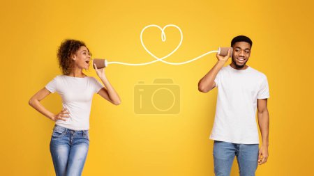 Photo for Language of love. Happy black guy listening to his girlfriend through can phone, orange studio background - Royalty Free Image