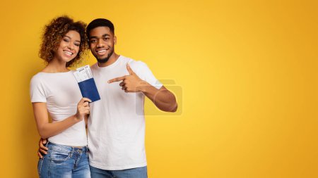 Foto de Feliz pareja afroamericana joven de turistas sonriendo y sosteniendo pasaportes y boletos, fondo naranja - Imagen libre de derechos