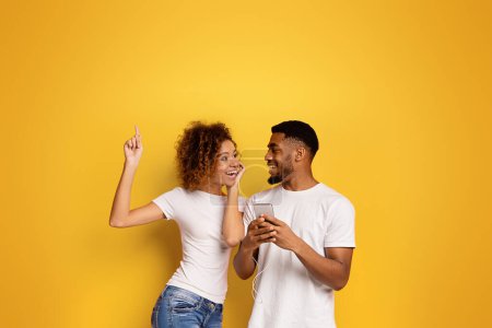 Foto de Feliz pareja afroamericana bailando juntos y apuntando hacia arriba con una sonrisa juguetona sobre un vibrante fondo amarillo - Imagen libre de derechos