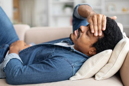 Photo for Black Man Feeling Unwell At Home, Suffering Stomach Pain And Headache, Upset African American Male Lying On Couch In Living Room, Closeup - Royalty Free Image