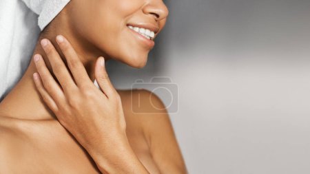 Foto de Chica afro-americana sonriente con hombros desnudos y toalla en la cabeza tocando su cuello, espacio para copiar. Concepto de spa diario - Imagen libre de derechos
