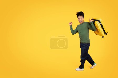 A delighted young african american man running and looking excited with a bright yellow suitcase on a vivid yellow background
