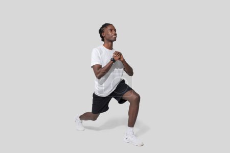 Black athletic guy is performing a lunge exercise, showing focus and strength, isolated on a white background