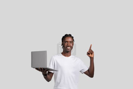 Photo for An african american man is shown standing and presenting something on a laptop screen, pointing upward, on an isolated white backdrop - Royalty Free Image