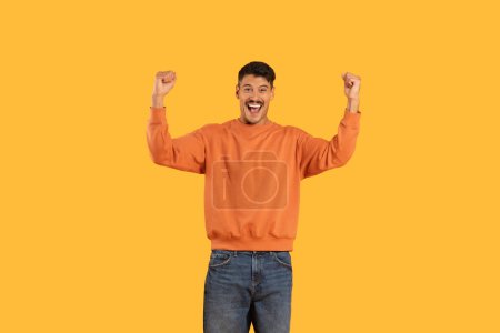 Cheerful man with a broad smile giving a double thumbs up sign for approval or success on yellow background