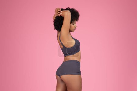 Photo for A back perspective of an african american sporty lady stretching her arms, accentuating isolated on mono-pink strength and elegance - Royalty Free Image