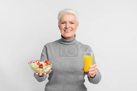 Foto de Anciana mujer europea equilibra una dieta saludable con ensalada y jugo, lo que representa una s3niorlife nutritiva - Imagen libre de derechos