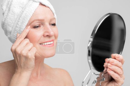 Photo for European elderly woman examines her skin while applying eye cream, a regular skincare part of preserving ones s3niorlife - Royalty Free Image