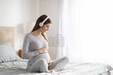 Foto de Una mujer europea embarazada acaricia su vientre, una escena tierna que refleja la suave preparación para la maternidad en casa - Imagen libre de derechos