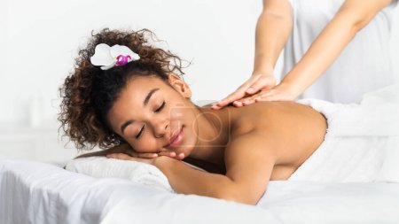 Photo for African-american girl enjoying back massage in spa salon, relaxing with closed eyes - Royalty Free Image