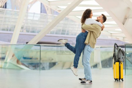 Téléchargez les photos : Homme aimant portant femme à l'aéroport après l'arrivée, la soulevant et l'embrassant, heureux couple romantique réunion après longtemps à part, Copier l'espace - en image libre de droit