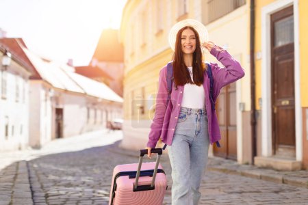 Photo for Joyful woman traveler with a pink suitcase strolling through a historic city, expressing travel and discovery - Royalty Free Image