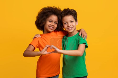 Photo for A pair of African American siblings make a heart shape with hands, symbolizing love and unity, against a warm yellow background - Royalty Free Image