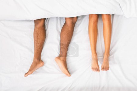 Photo for African-american couple legs under duvet laying on bed, top view - Royalty Free Image