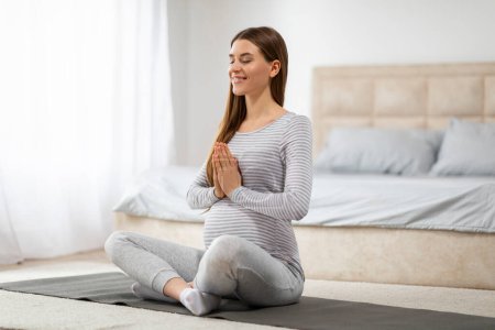 Téléchargez les photos : Une femme enceinte sereine est capturée dans un moment de pleine conscience, s'engageant dans le yoga prénatal sur un tapis dans un cadre lumineux et confortable chambre - en image libre de droit