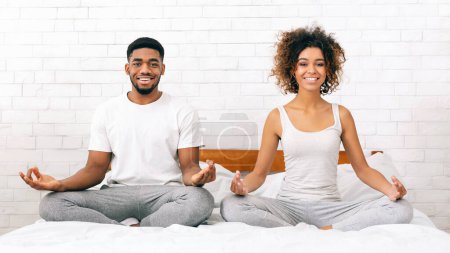 Active lifestyle. Cheerful african-american man and woman sitting in lotus position on bed, copy space