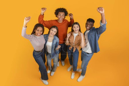 Photo for Generation Z friends with multiracial and multiethnic backgrounds raise their fists in triumph and excitement on an orange background - Royalty Free Image