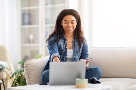 Photo for An african american lady enjoys browsing on her laptop, sitting comfortably at home, exhibiting joy and relaxation - Royalty Free Image